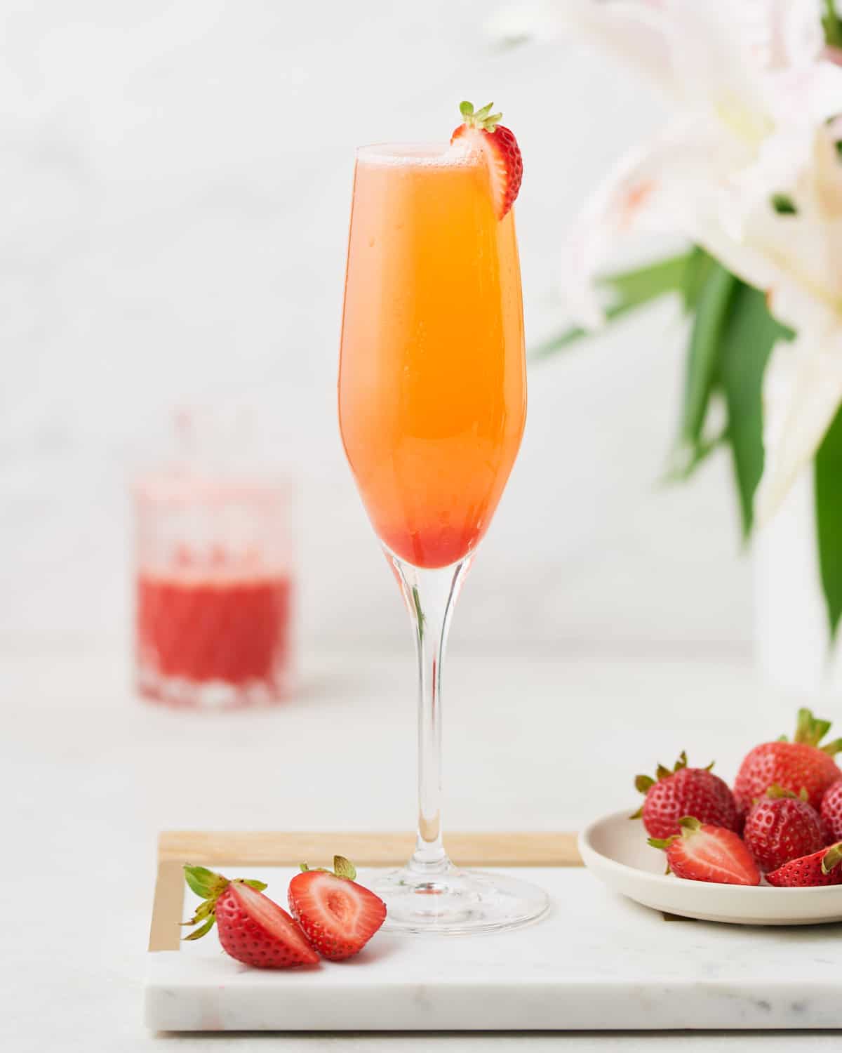 Side view of Rossini Cocktail on a marble surface with cut strawberries.