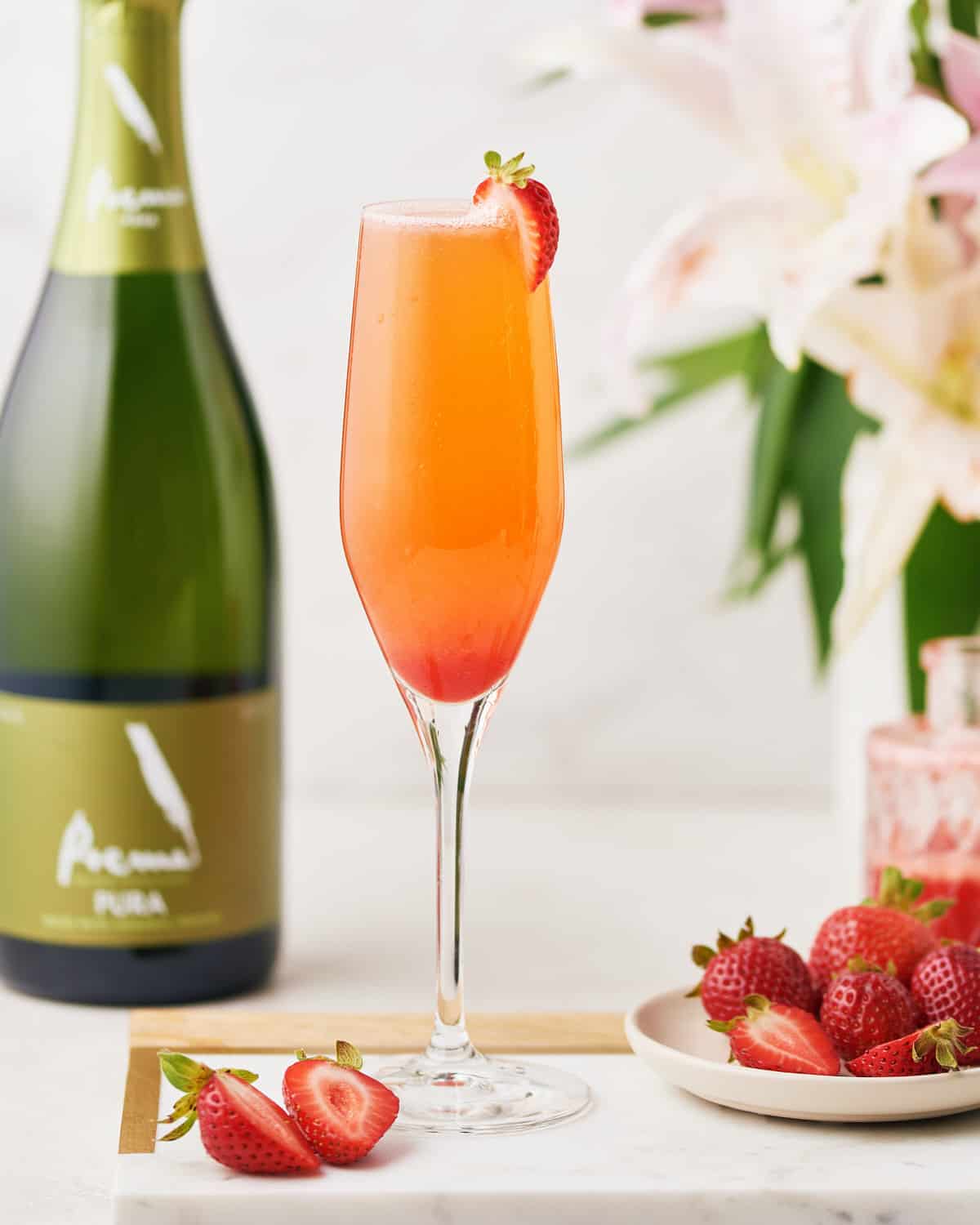 Side view of Rossini Cocktail with bottle of Cava and sliced strawberries.