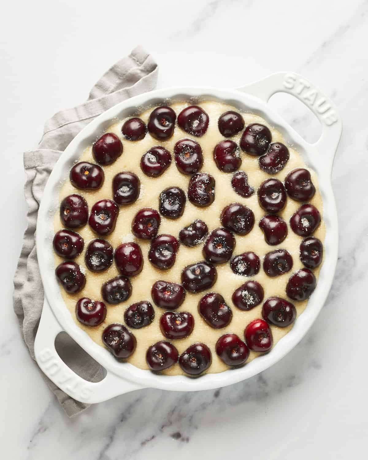 Overhead view of batter in a baking dish with fresh sweet cherries and sugar sprinkled on top.