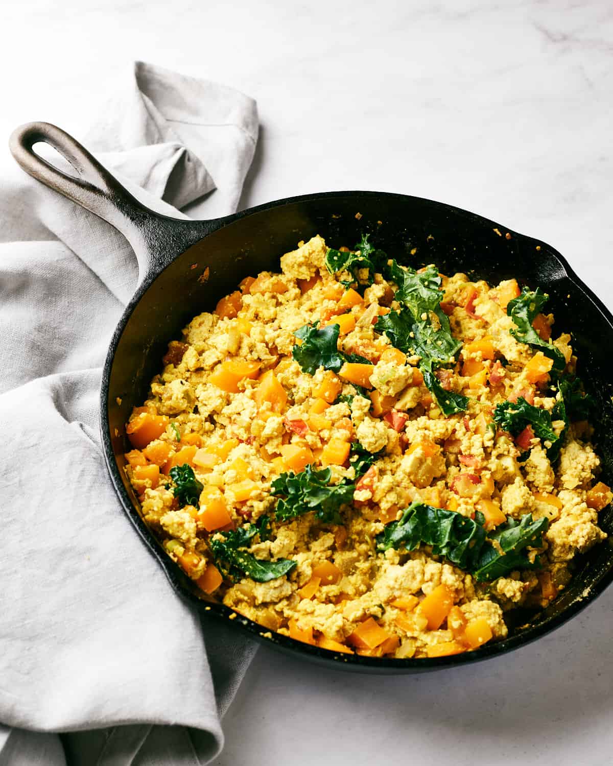 Side angle view of Easy Vegan Southwestern Tofu Scramble in Cast Iron Skillet on a marble surface.