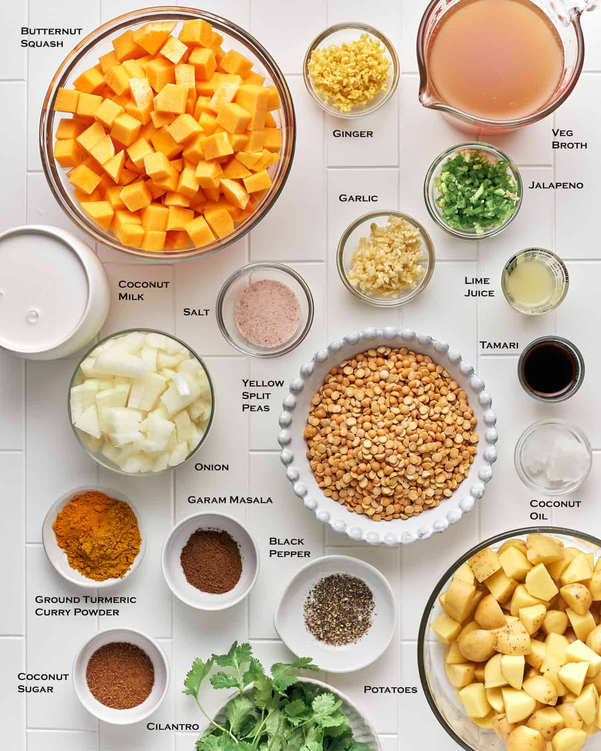 Overhead view of ingredients to make vegan butternut squash curry soup with potatoes on a white tile background.