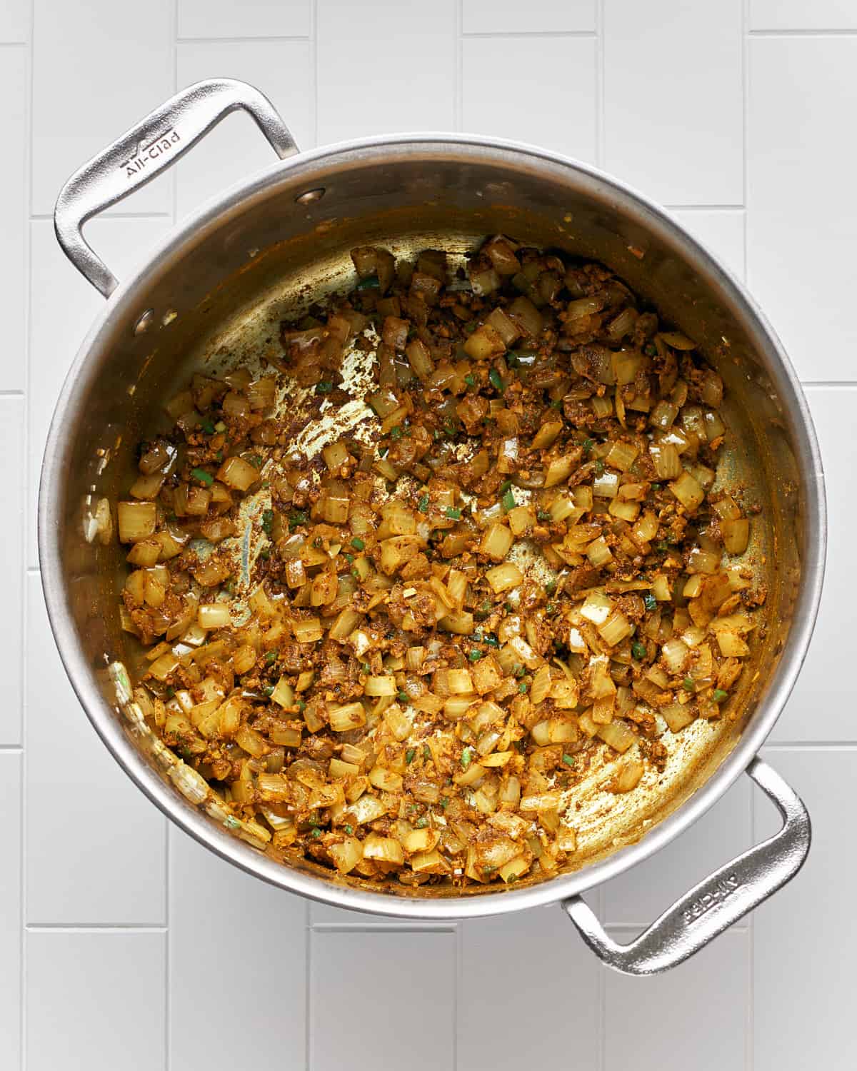 Overhead view of cooking onions, garlic and ginger in a large stainless steel pot with spices.