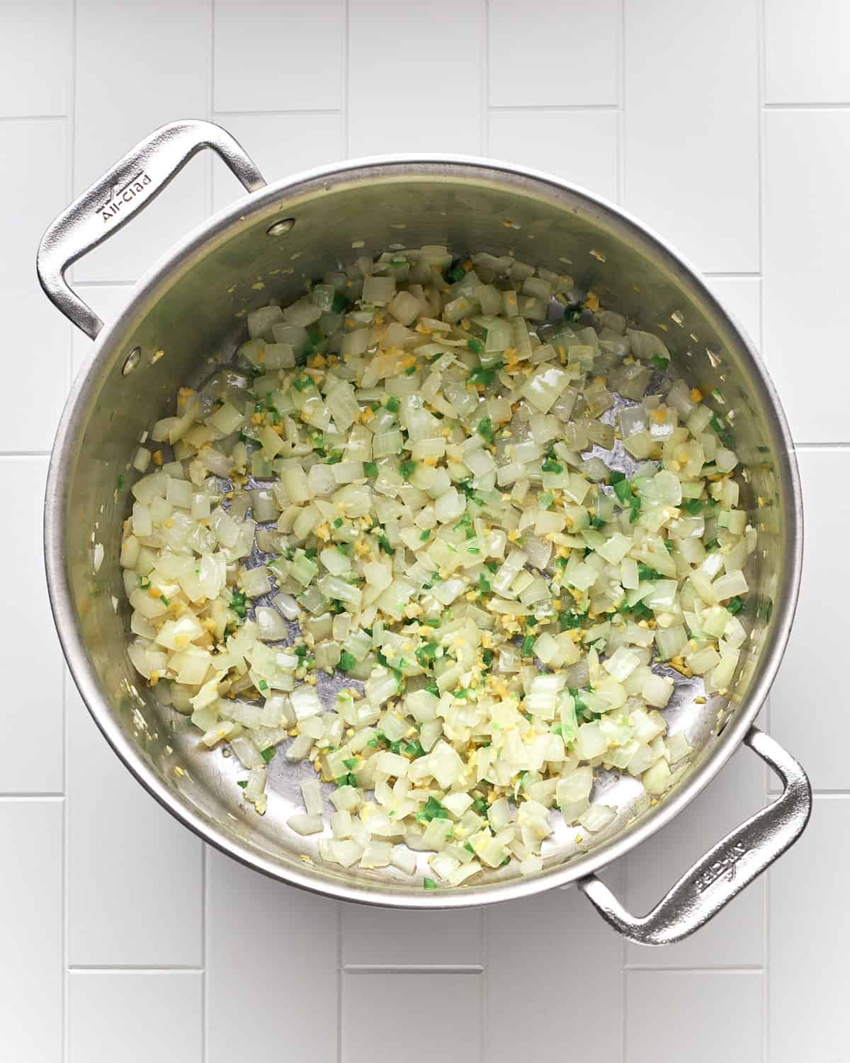 Overhead view of sauteeing onions, jalapeno pepper, garlic, and ginger in large stainless steel pot to make butternut squash curry soup.