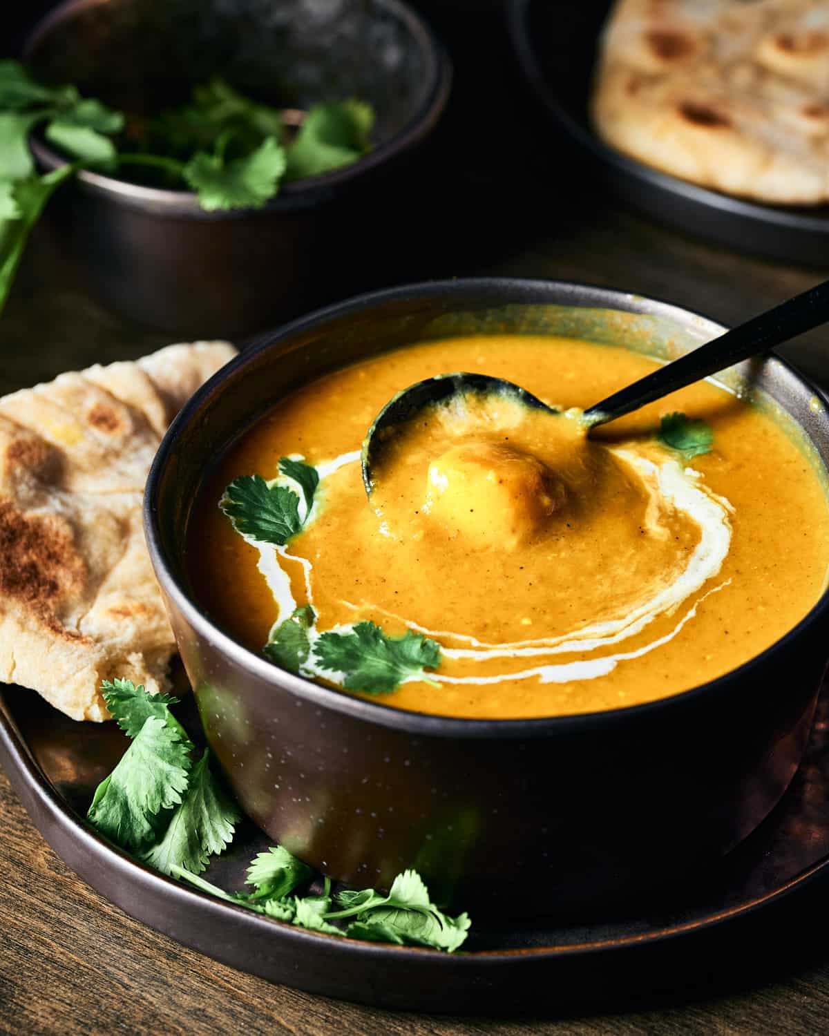 Side view of vegan butternut squash curry soup garnished with swirl of coconut milk and fresh cilantro with spoon in bowl.