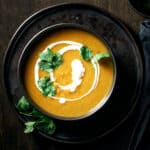 Overhead view of vegan butternut squash curry soup garnished with swirl of coconut milk and fresh cilantro.