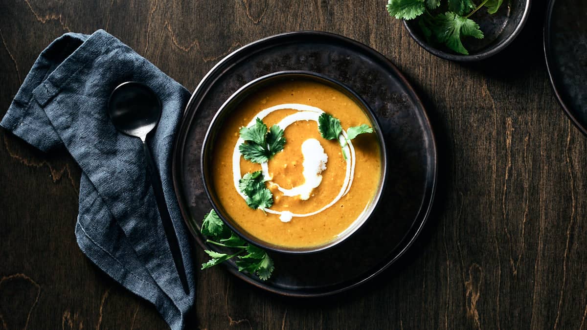 Overhead view of vegan butternut squash curry soup garnished with swirl of coconut milk and fresh cilantro.