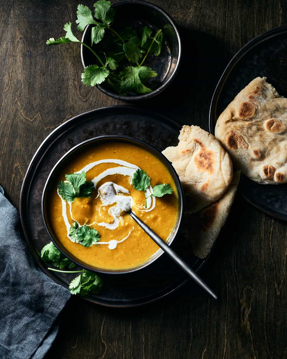Overhead view of vegan butternut squash curry soup garnished with swirl of coconut milk and fresh cilantro, with naan on the side on a plate.