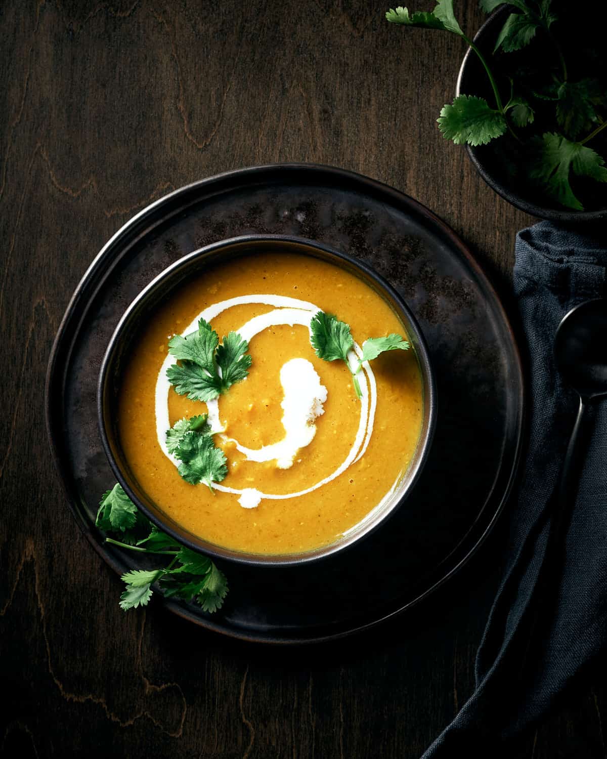 Overhead view of vegan butternut squash curry soup garnished with swirl of coconut milk and fresh cilantro.