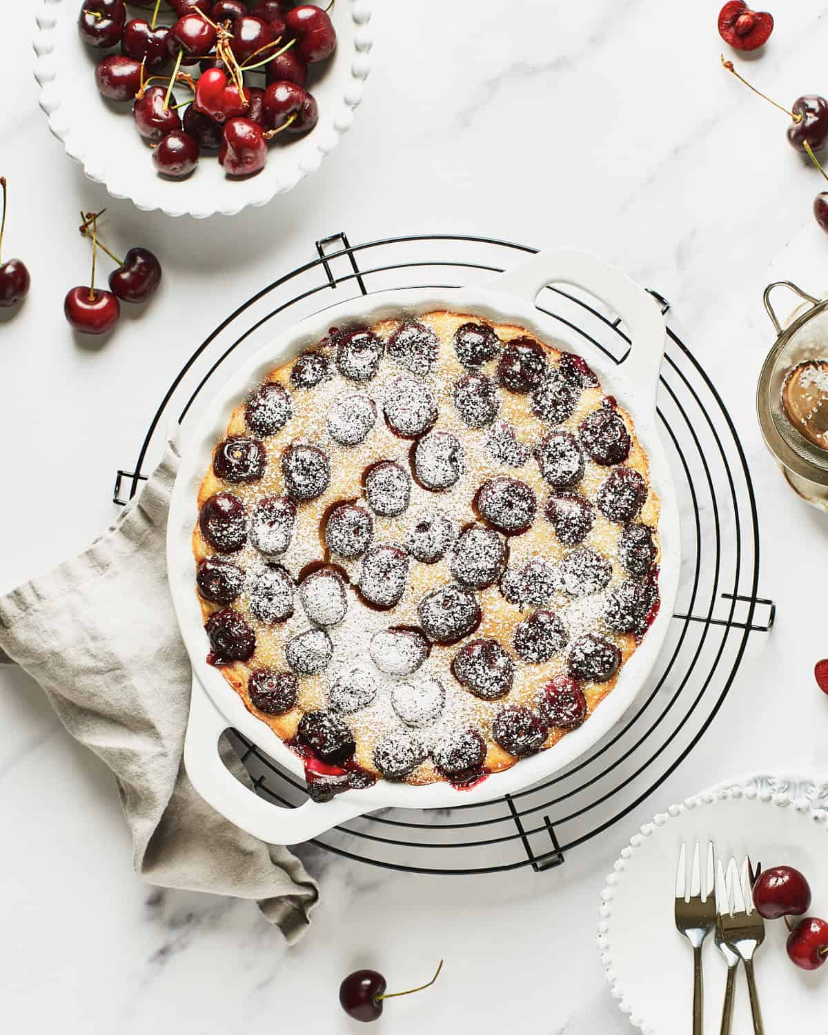 Overhead view of Vegan Clafoutis or Clafoutis Vegano with a slice on a white plate with a small bowl of cherries.
