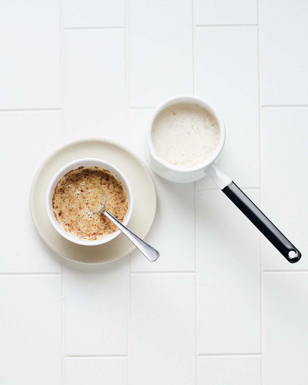 Overhead view of flaxseed meal in a bowl mixed with orange juice and soymilk with apple cider vinegar next to it on a white tile surface.