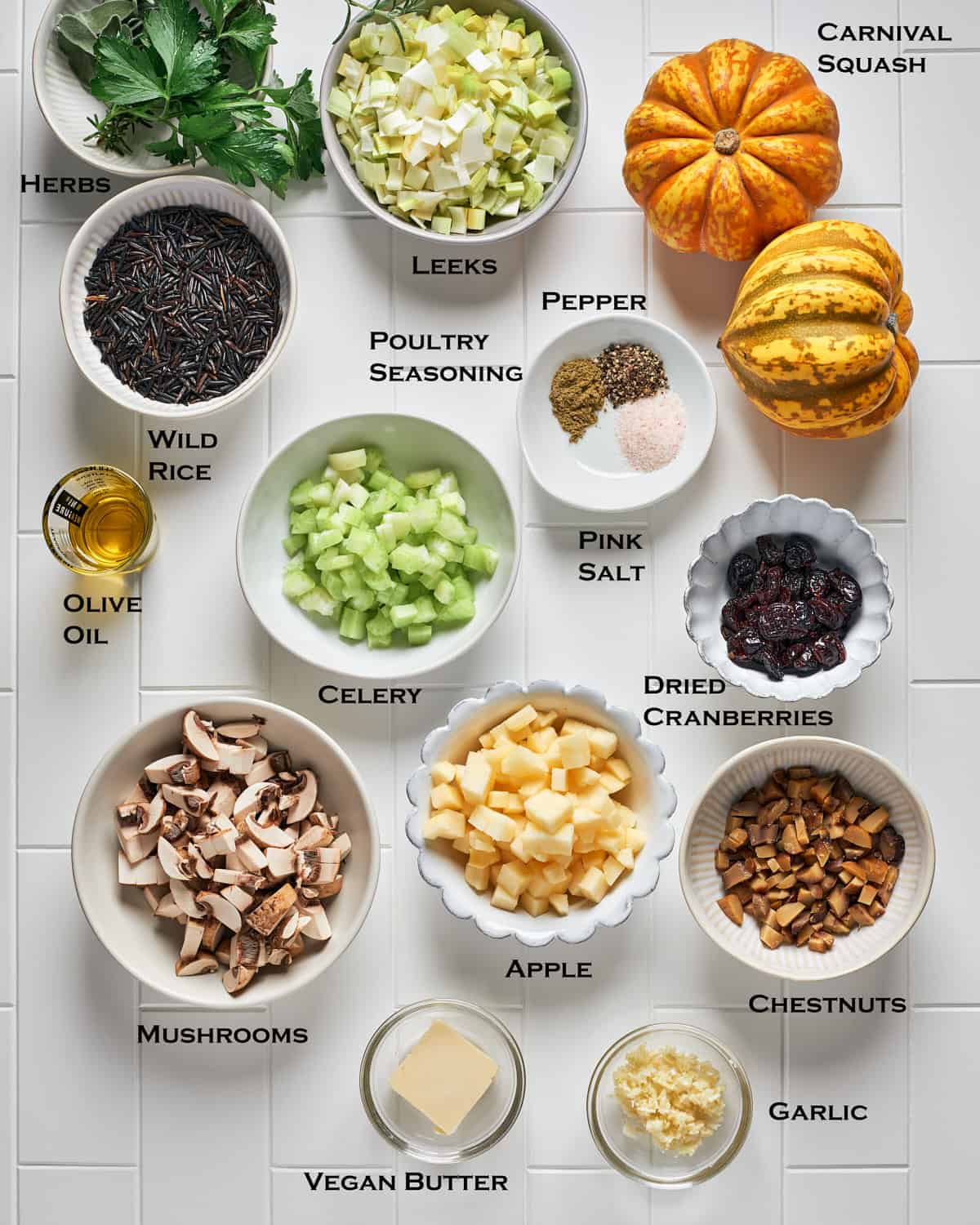 Ingredients to make Stuffed Carnival Squash with Wild Rice, Mushrooms, and Leeks on a white tile surface.