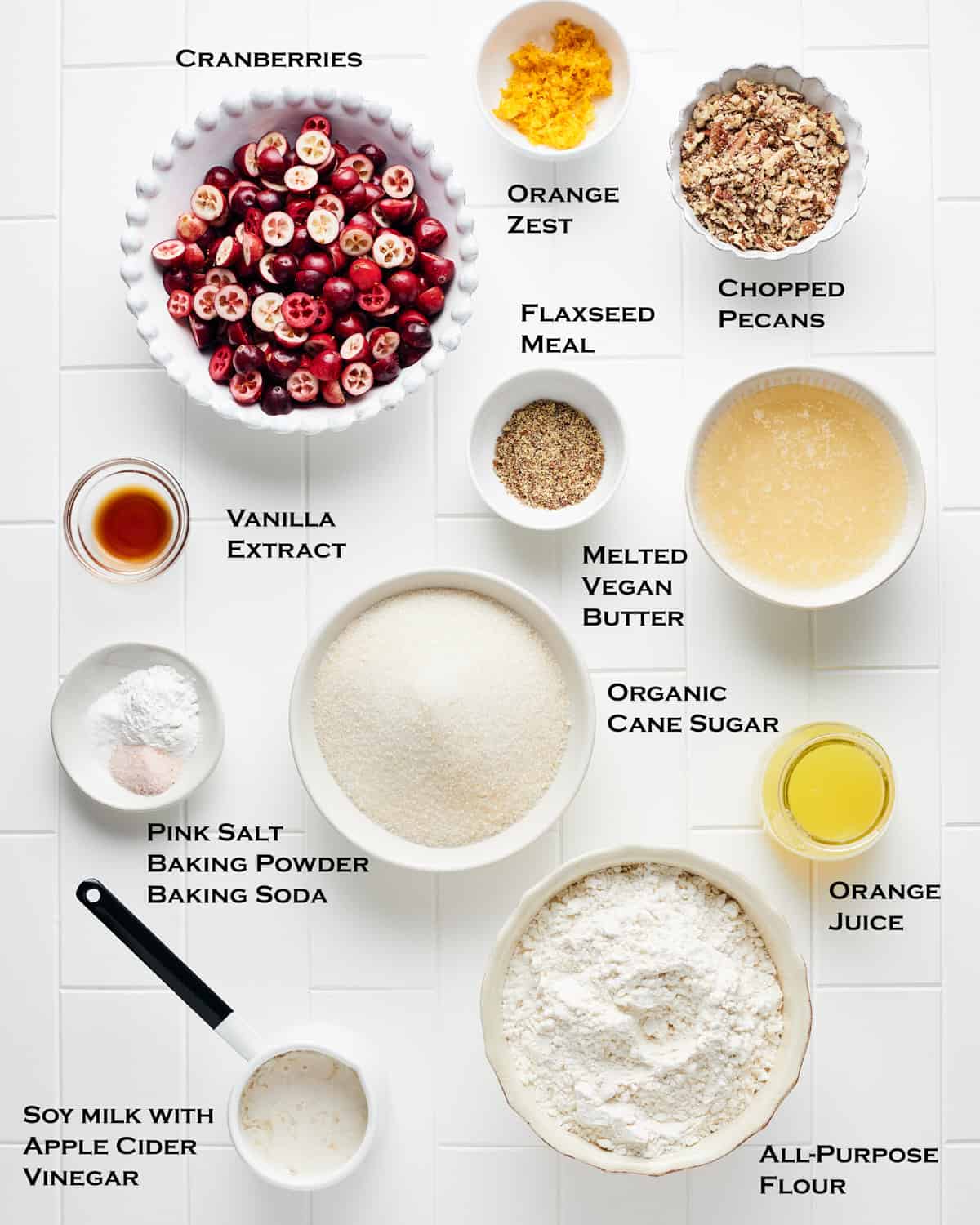 Overhead view of ingredients to make vegan cranberry orange bread on a white tile surface.
