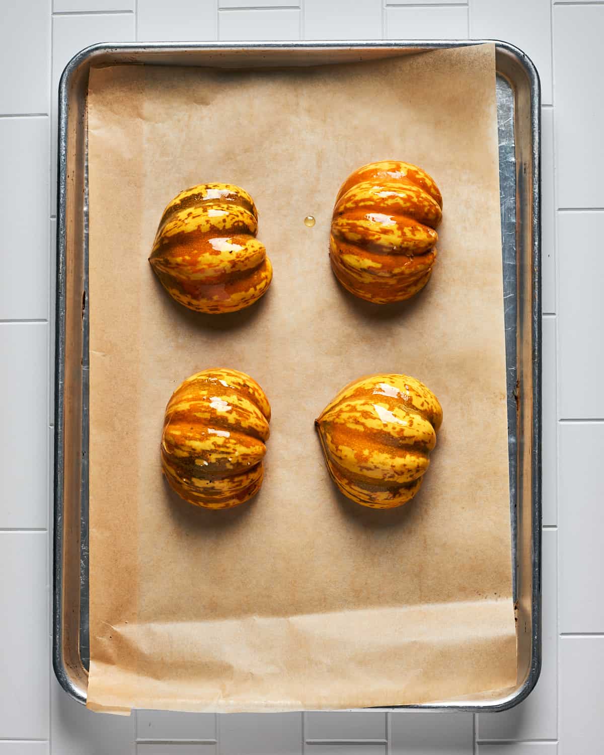 Overhead view of oiled carnival squash halves with salt and pepper on parchment paper on baking sheet before going in oven.