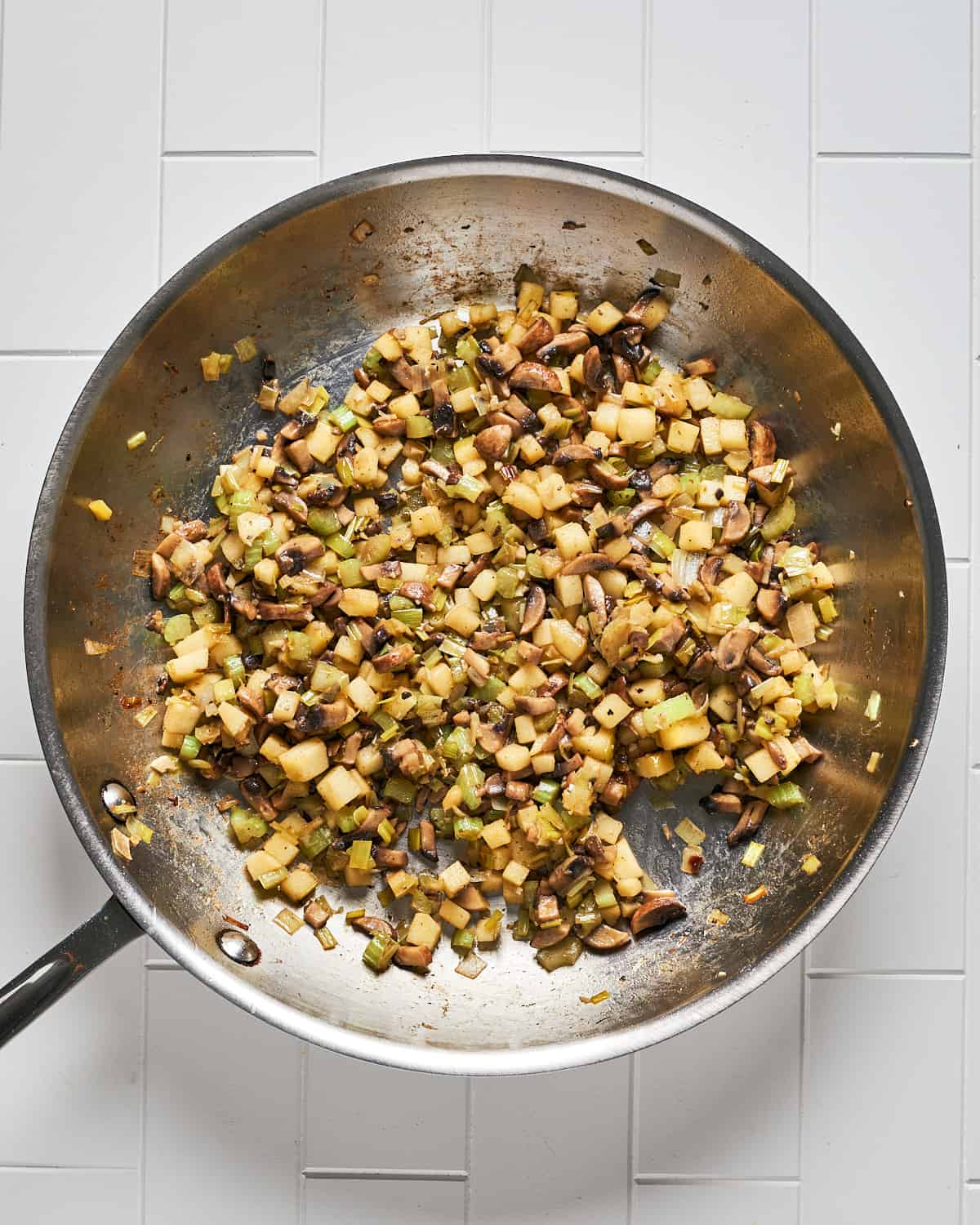 Overhead view of cooked leeks, mushroom, apple, and garlic in large skillet.