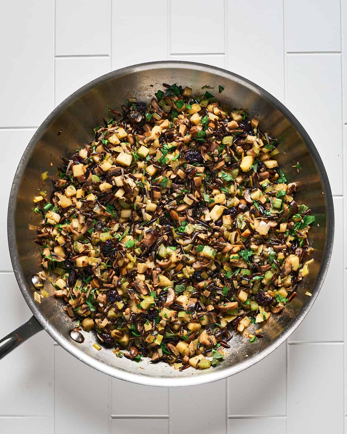 Overhead view of stuffing in skillet on white tile surface.
