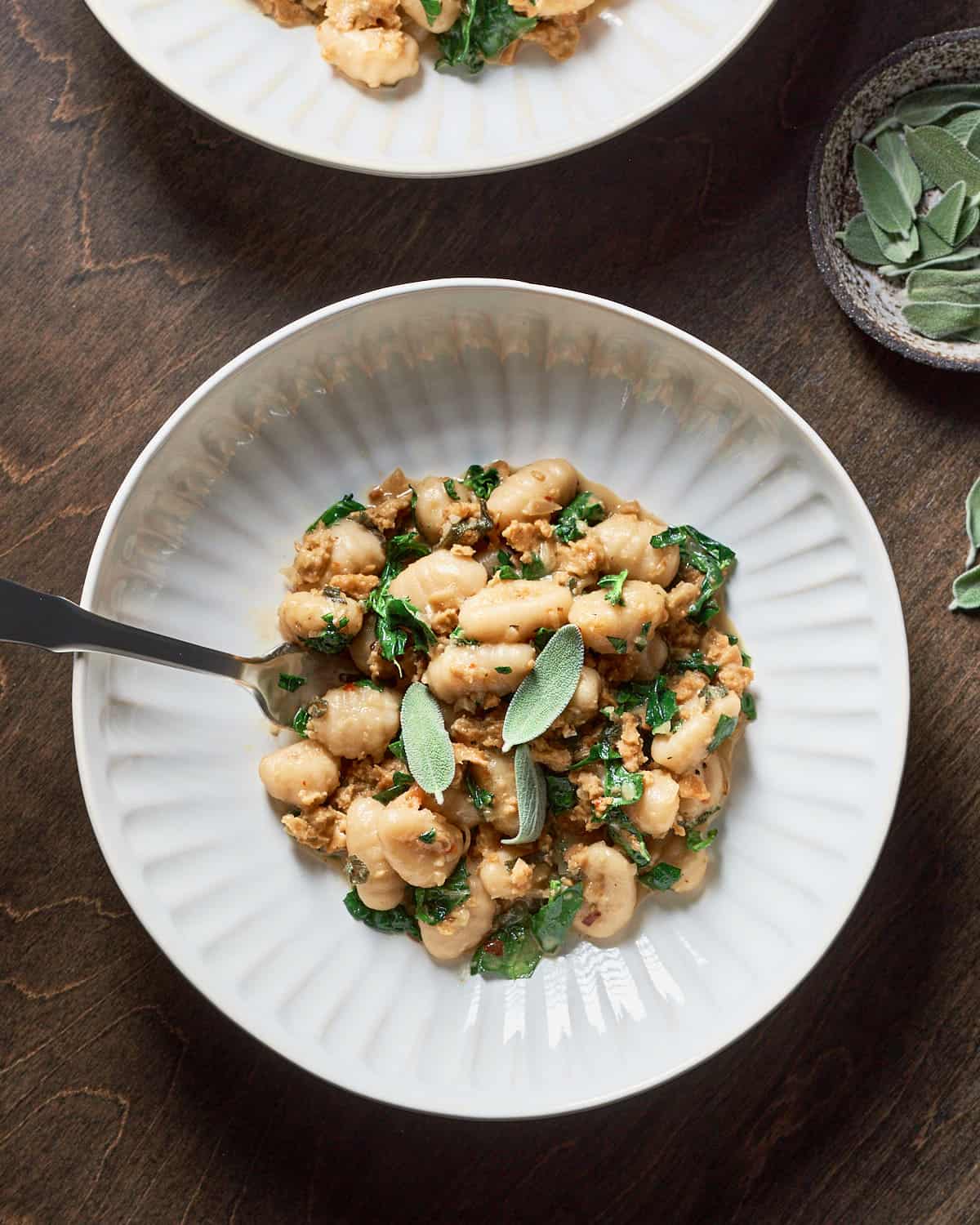 Overhead view of vegan gnocchi with sausage and kale on a wood background.