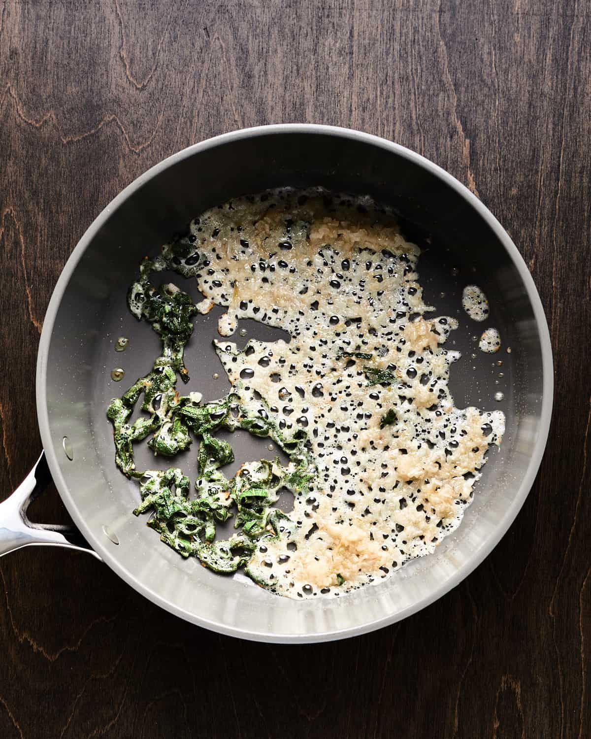 Overhead view of sauteing shallot and kale in saucepan.