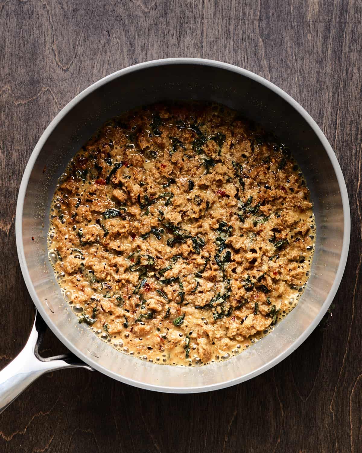Overhead view of cooking shallot, sage, kale, and vegan sausage in saucepan with vegan butter.
