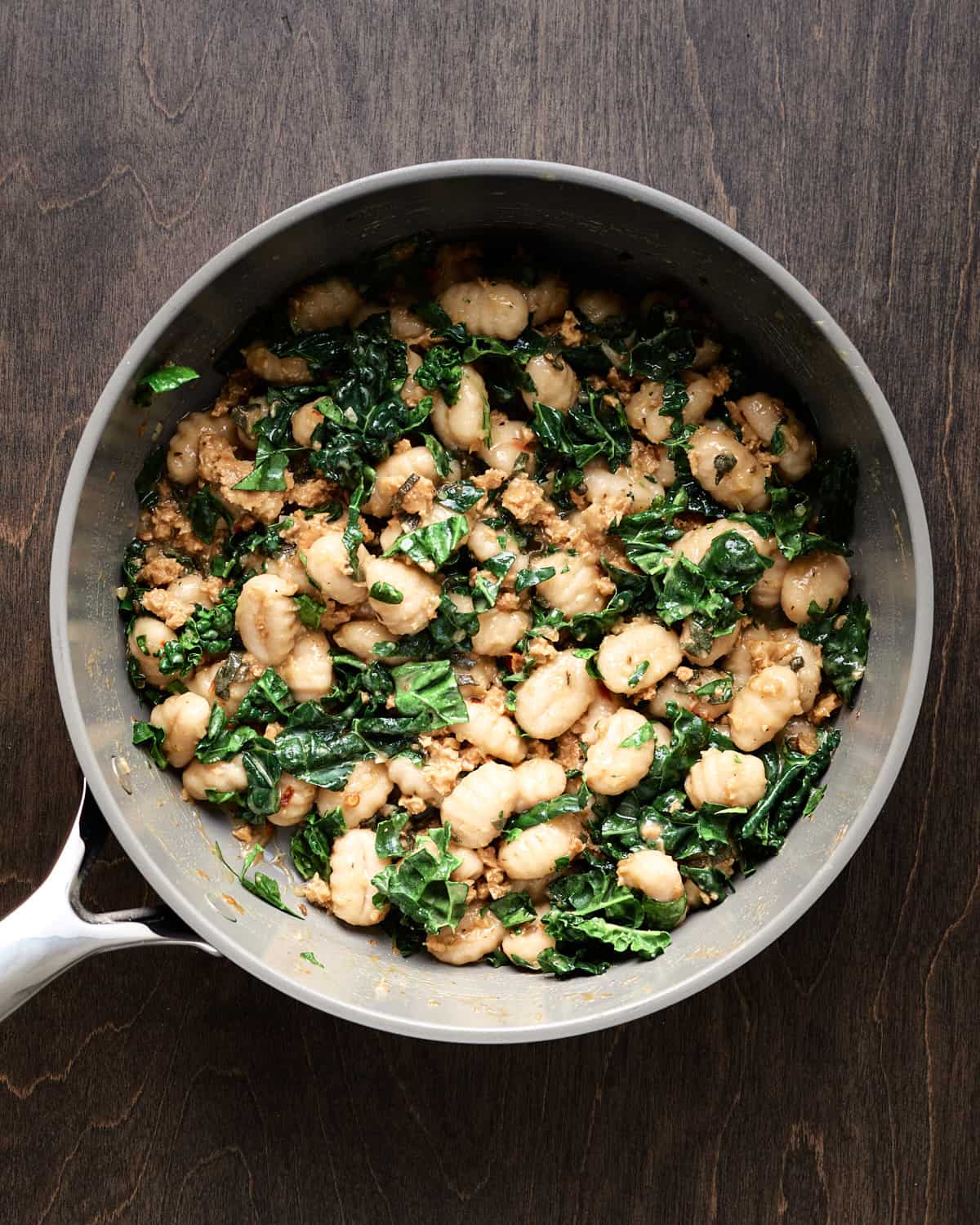 Overhead view of cooked vegan gnocchi with sausage and kale in saucepan.