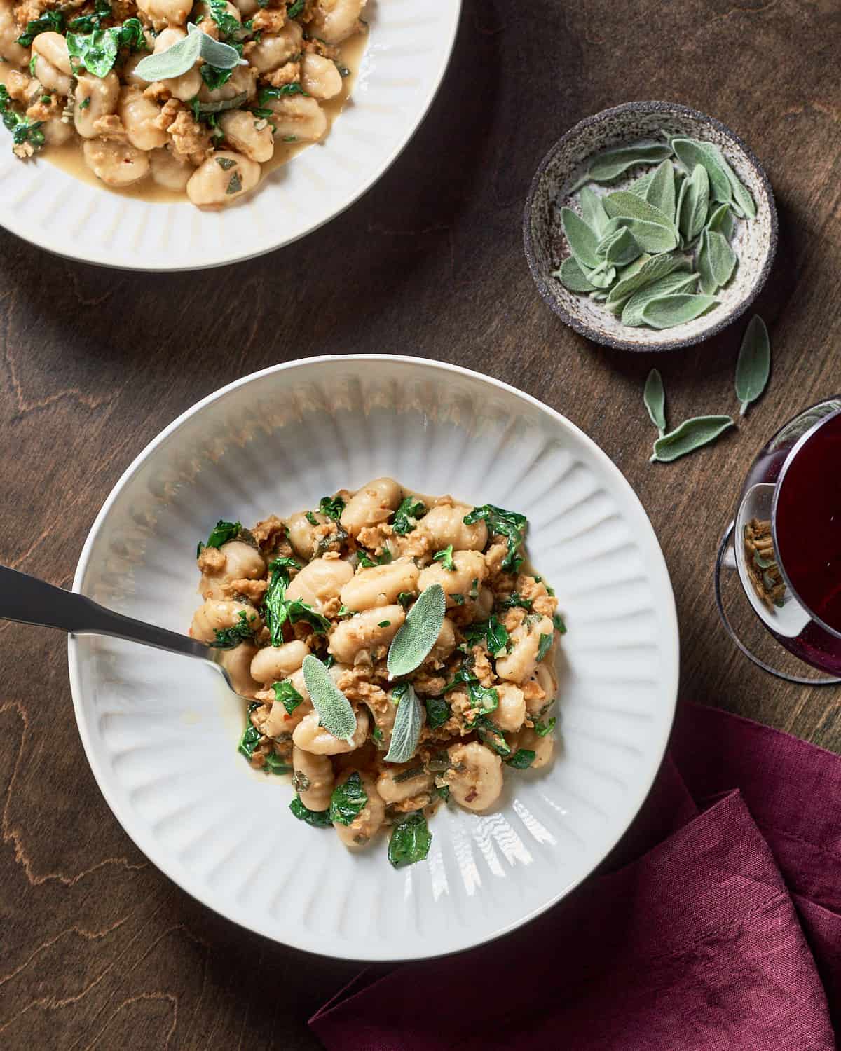 Overhead view of vegan gnocchi with sausage and kale on a wood background.