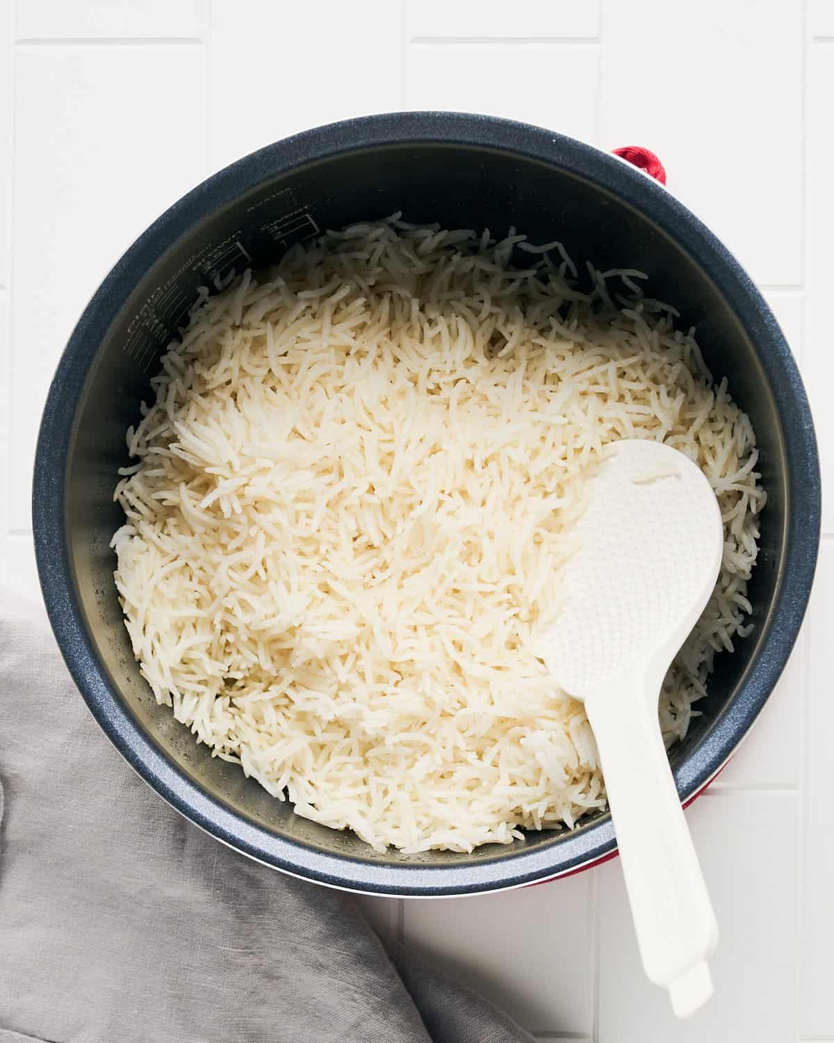 Overhead view of cooked long grain white rice in rice cooker pot with rice paddle.
