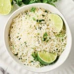 Rice cooker cilantro lime rice in a bowl on a serving platter with lime and cilantro.
