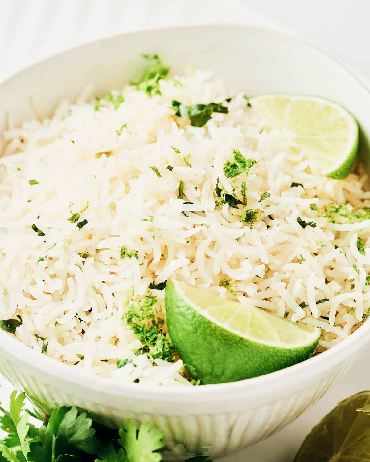 Overhead view of rice cooker cilantro lime rice in a bowl on a serving platter with lime and cilantro.