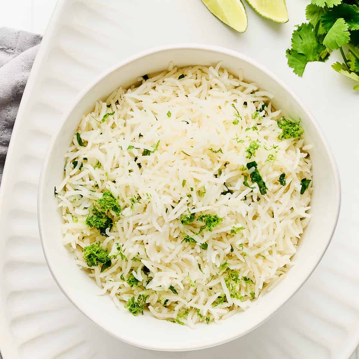 Overhead view of rice cooker cilantro lime rice in a bowl on a serving platter with lime and cilantro.