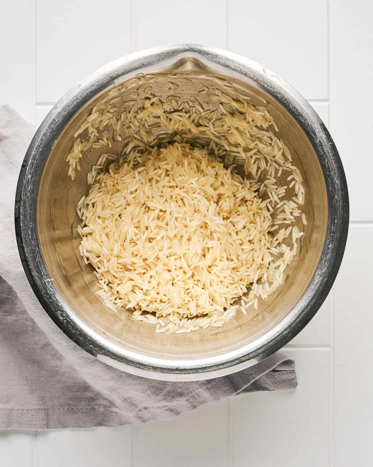 Overhead view of Rinsed Long Grain White Rice in a Bowl on a white tile surface.