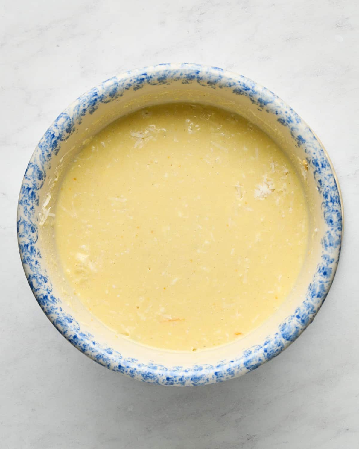 Overhead view of JUST Egg Frittata batter in a blue and white mixing bowl on a marble surface.