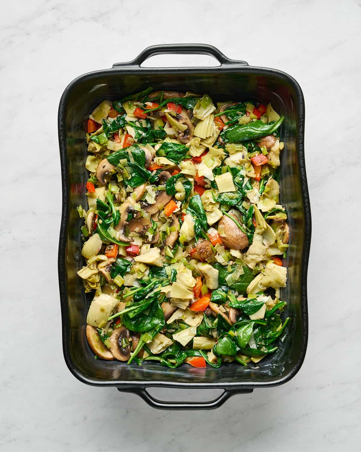 A black baking dish with cooked vegetables as the first layer.