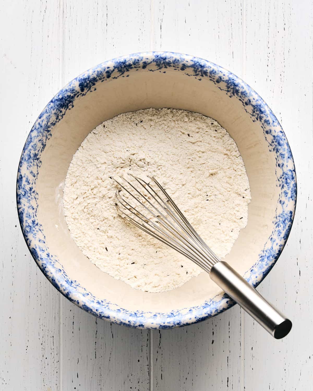 Dry ingredients in a large bowl with a mix on a white wooden surface.