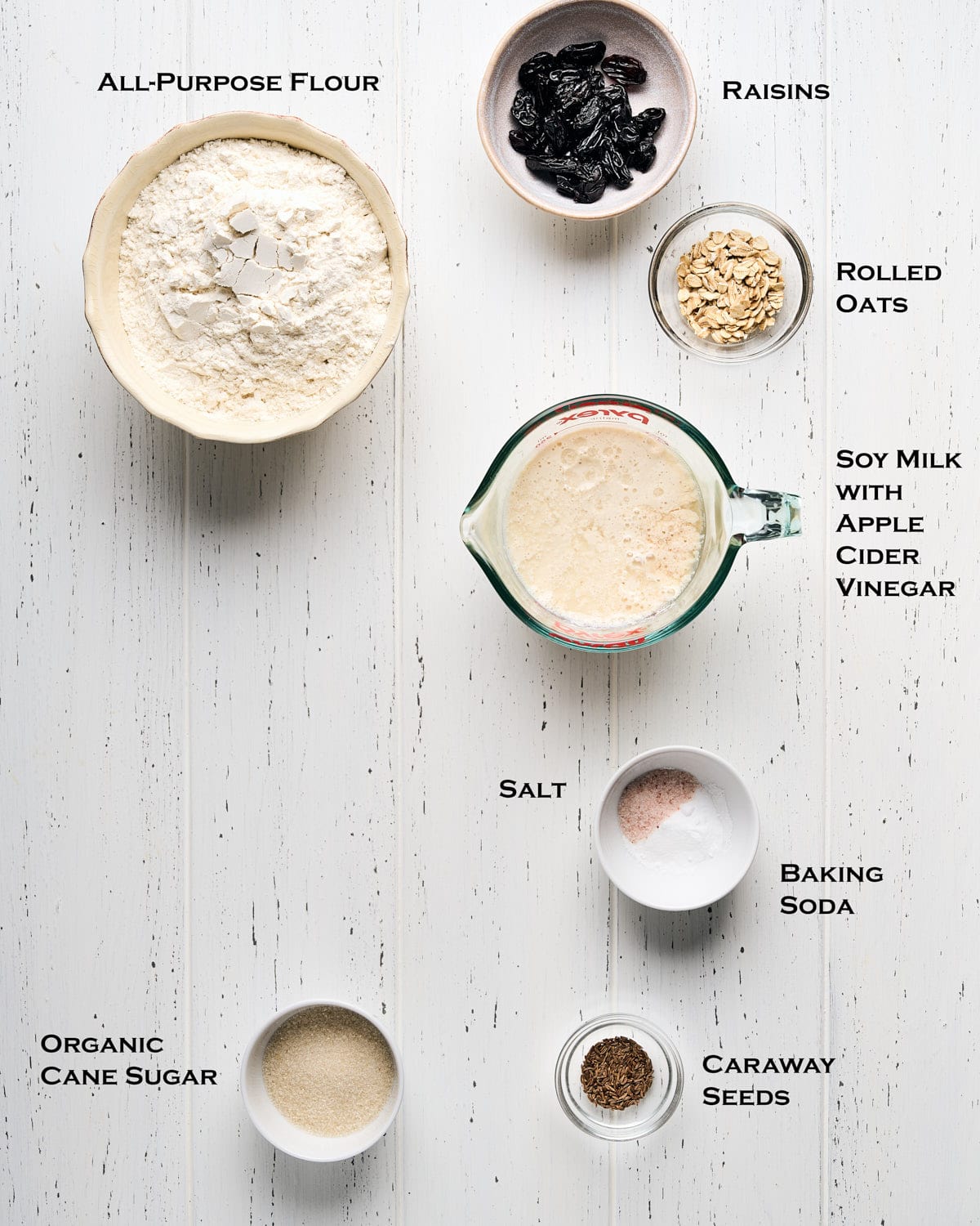 Ingredients to make vegan Irish soda bread laid out on a white wooden surface.