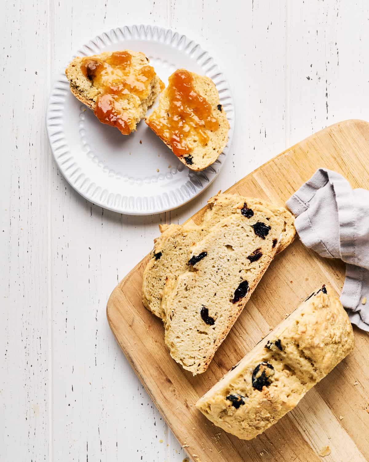 Sliced Vegan Irish Soda Bread on a cutting board next to a plate with buttered bread with jam.
