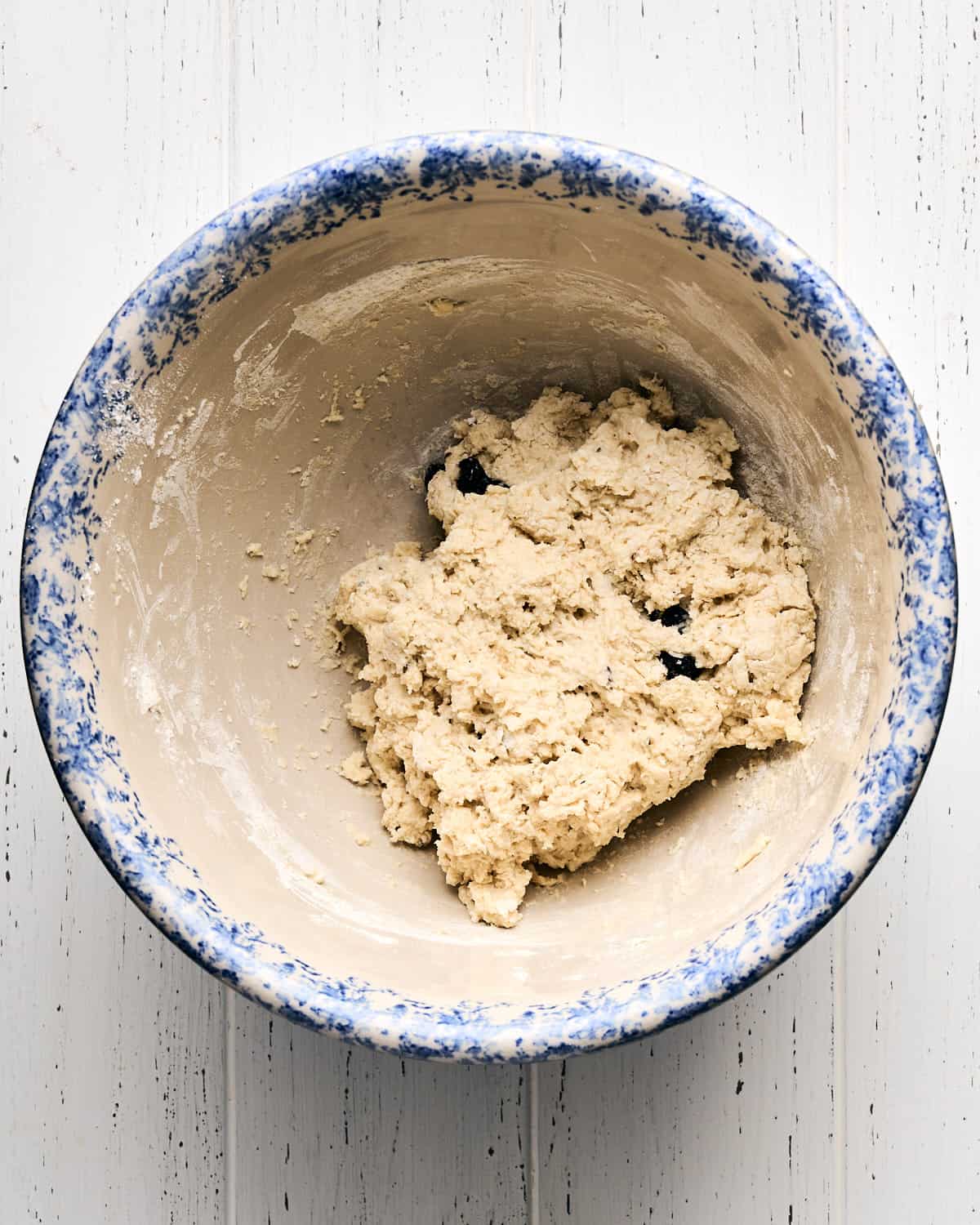 Mixing the dough in a large bowl with raisins on a white wooden surface.
