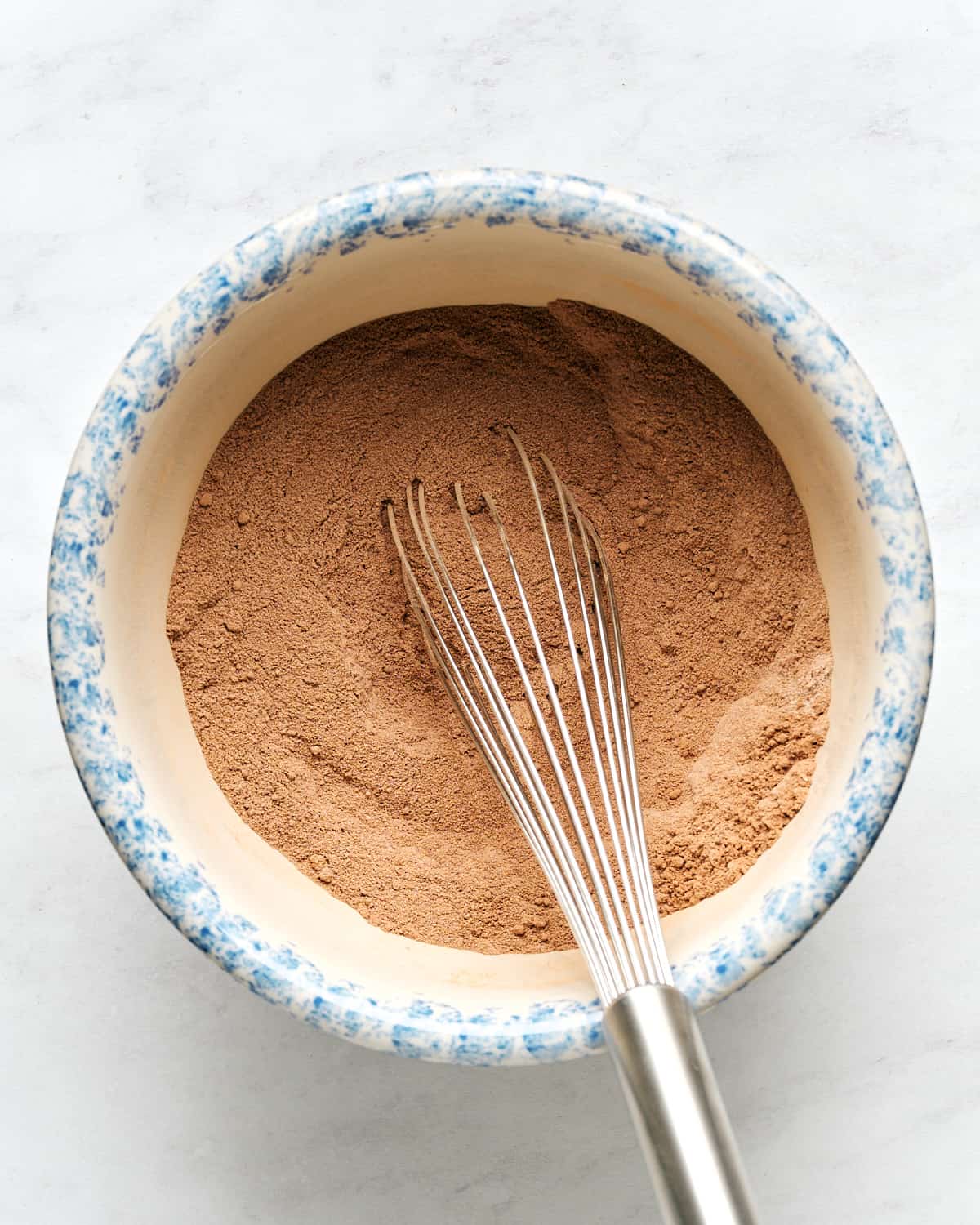 Mixing dry ingredients in a large bowl with a whisk on a marble surface.