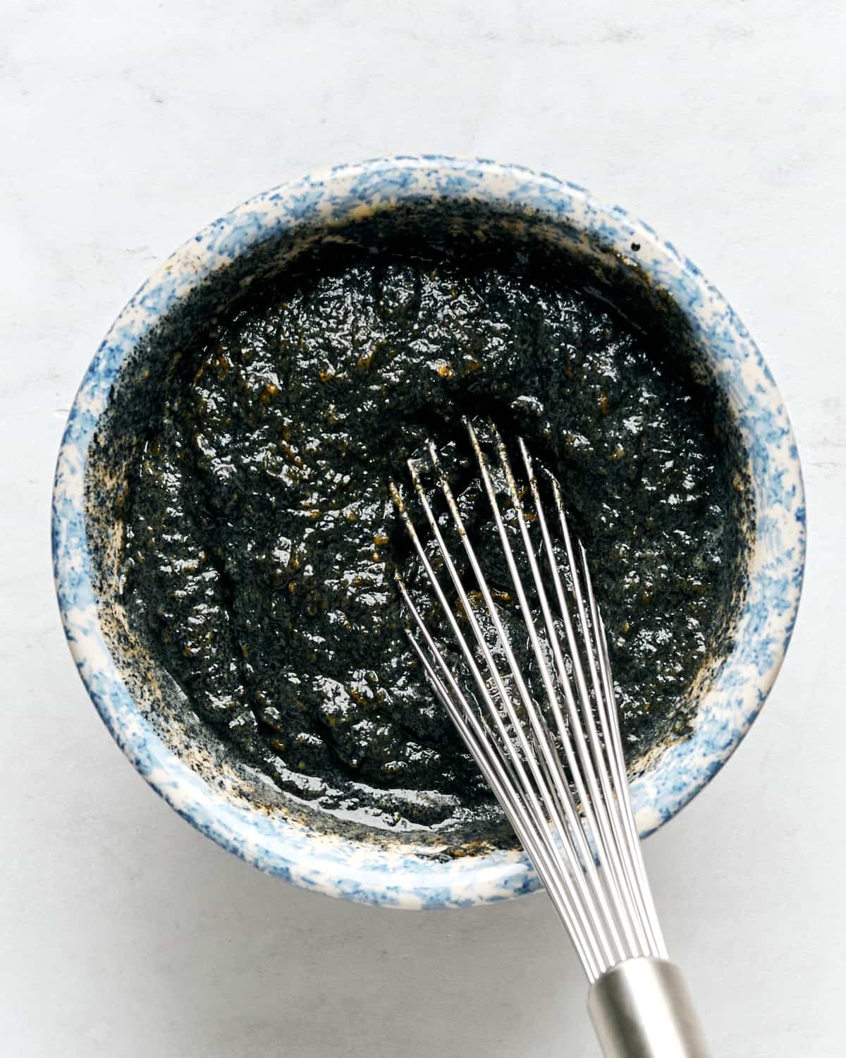 Mixing wet ingredients in a medium bowl with a whisk on a marble surface.