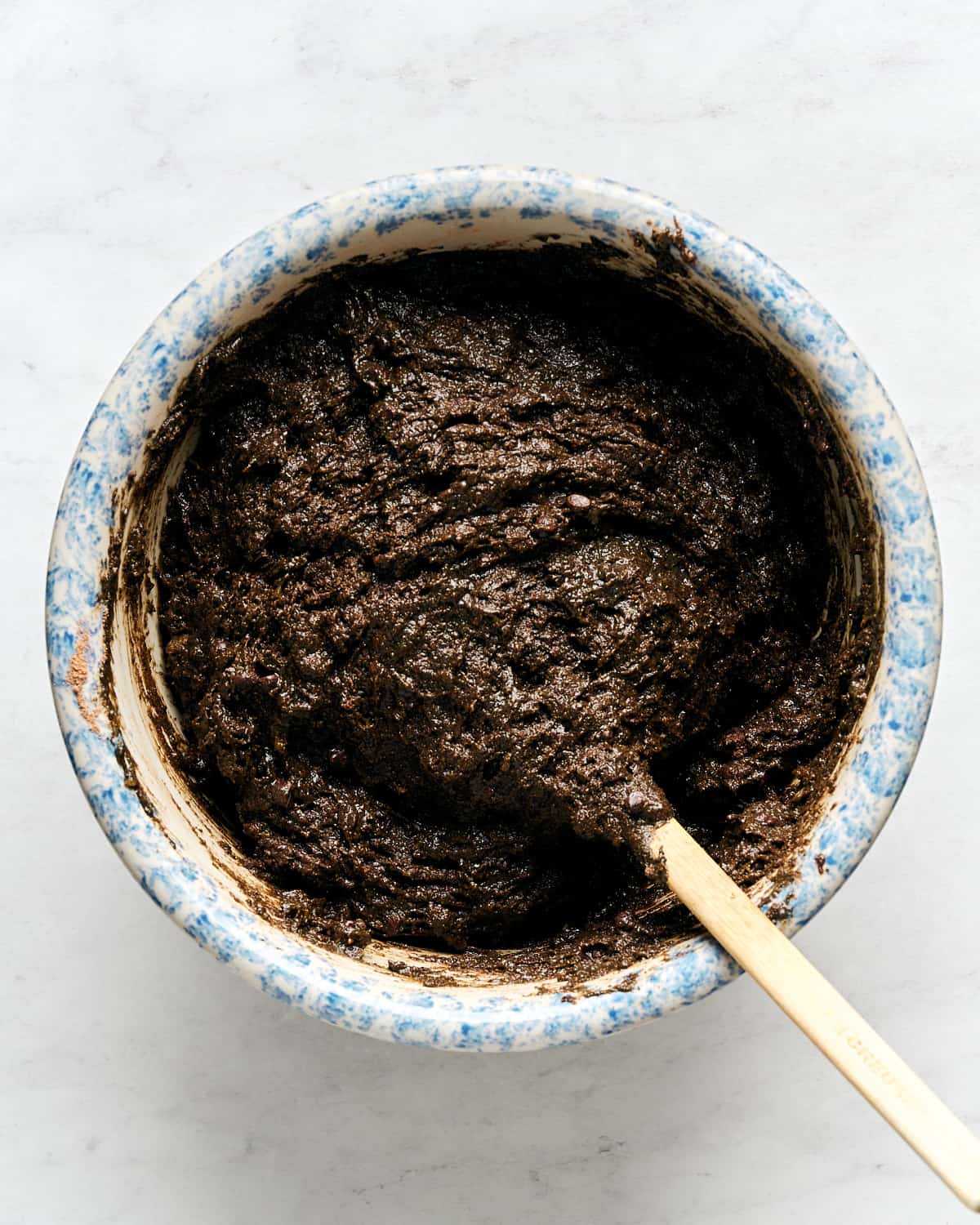 Mixing wet and dry ingredients in a large bowl with chocolate chips with a spatula.
