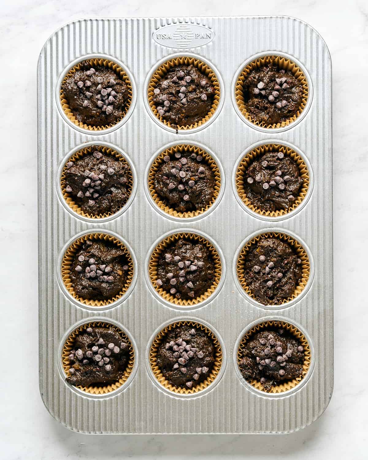 Muffin batter poured into liners in a muffin pan on a marble surface.
