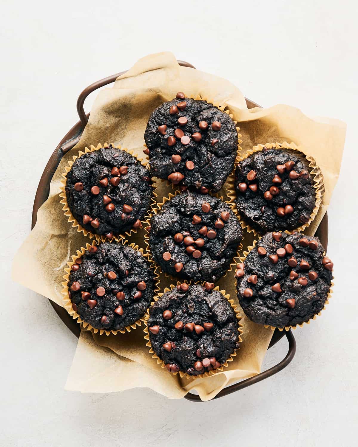 A round tray with seven vegan chocolate sweet potato muffins on parchment paper.