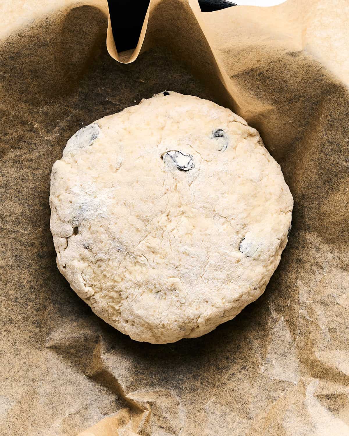 Unbaked dough in a round shape placed on parchment paper in a 9-inch cast iron pan on a white wooden surface.
