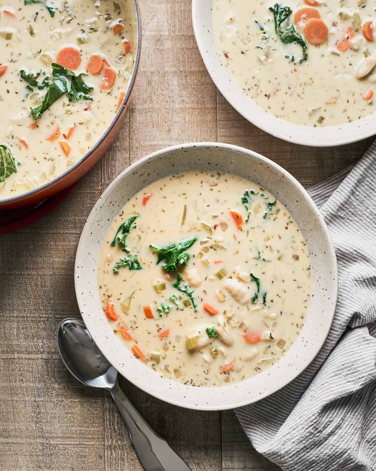 Two bowls and a large pot filled with vegan gnocchi soup with a napkin and spoons nearby.
