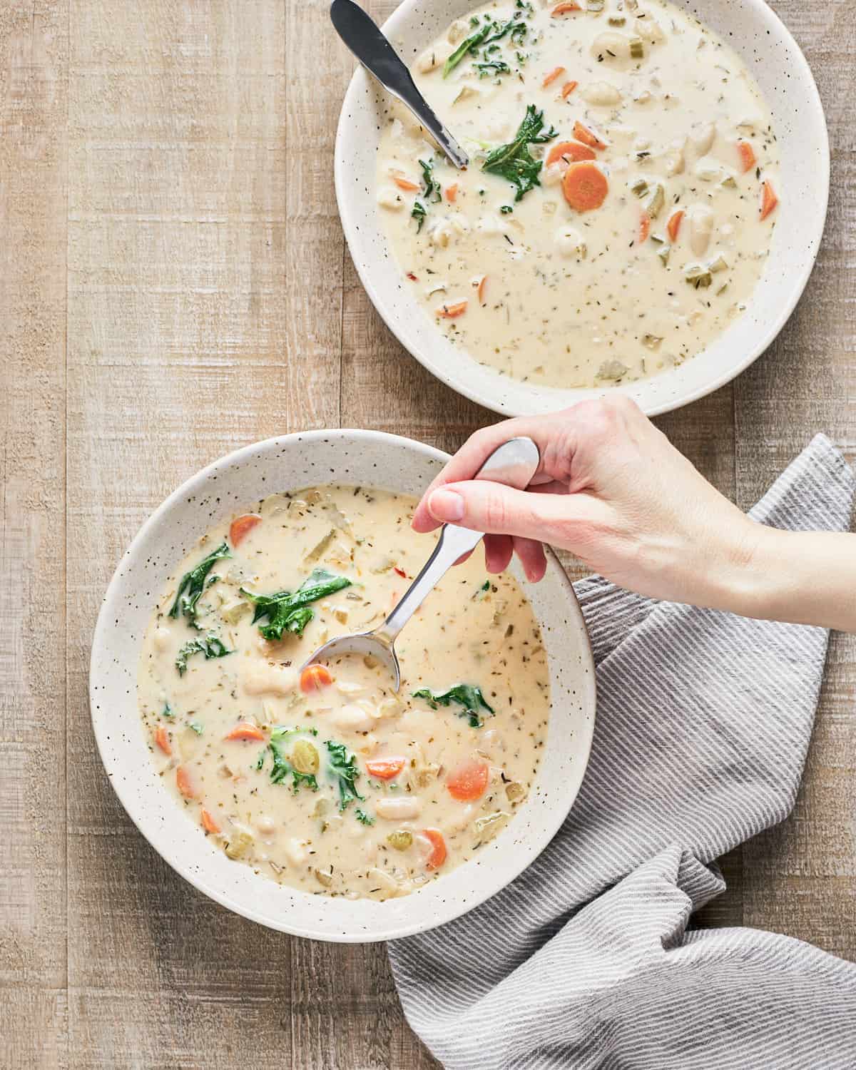Two bowls of gnocchi soup with a female hand holding a spoon and a napkin nearby.