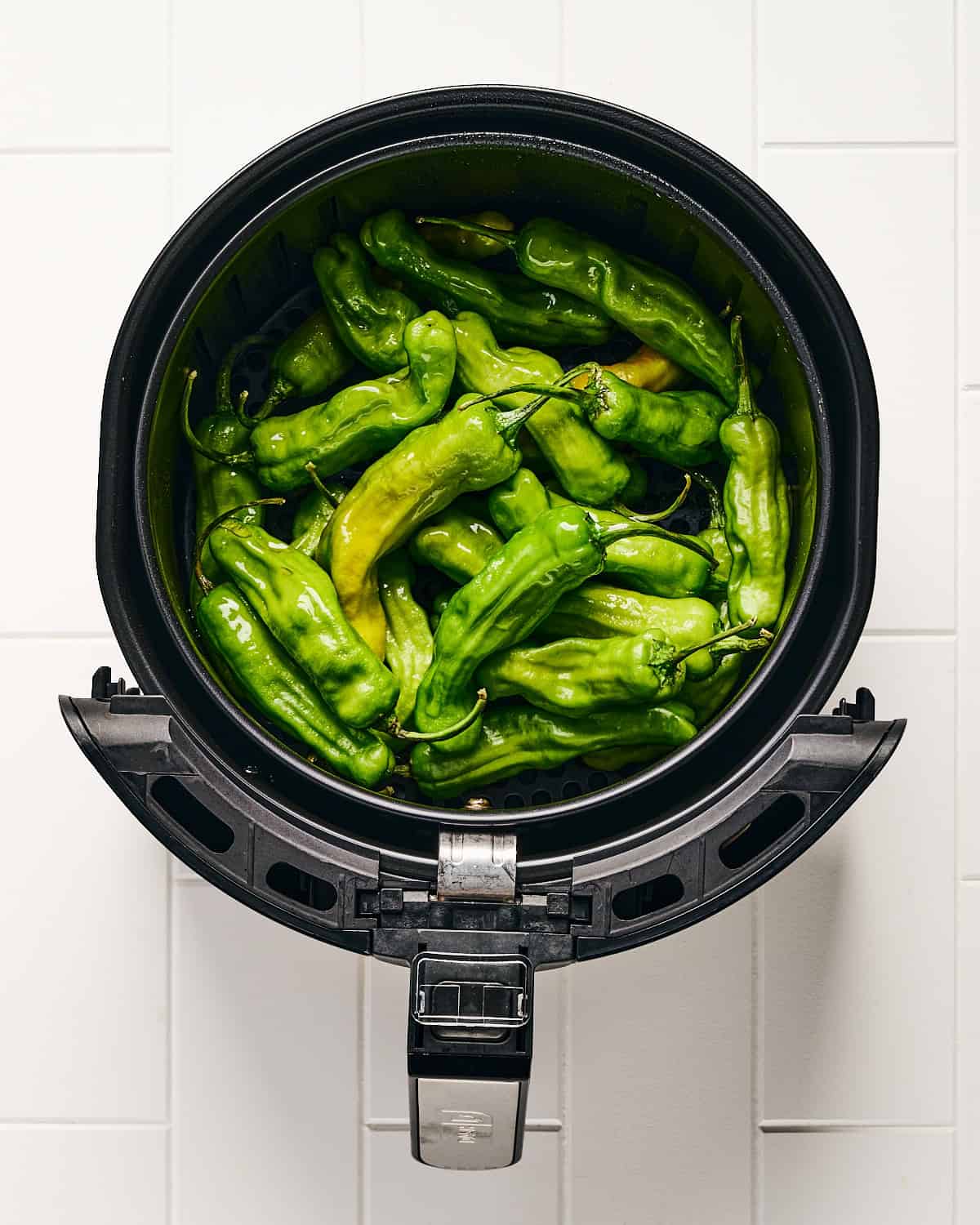 Uncooked and oiled shishito peppers in air fryer basket.