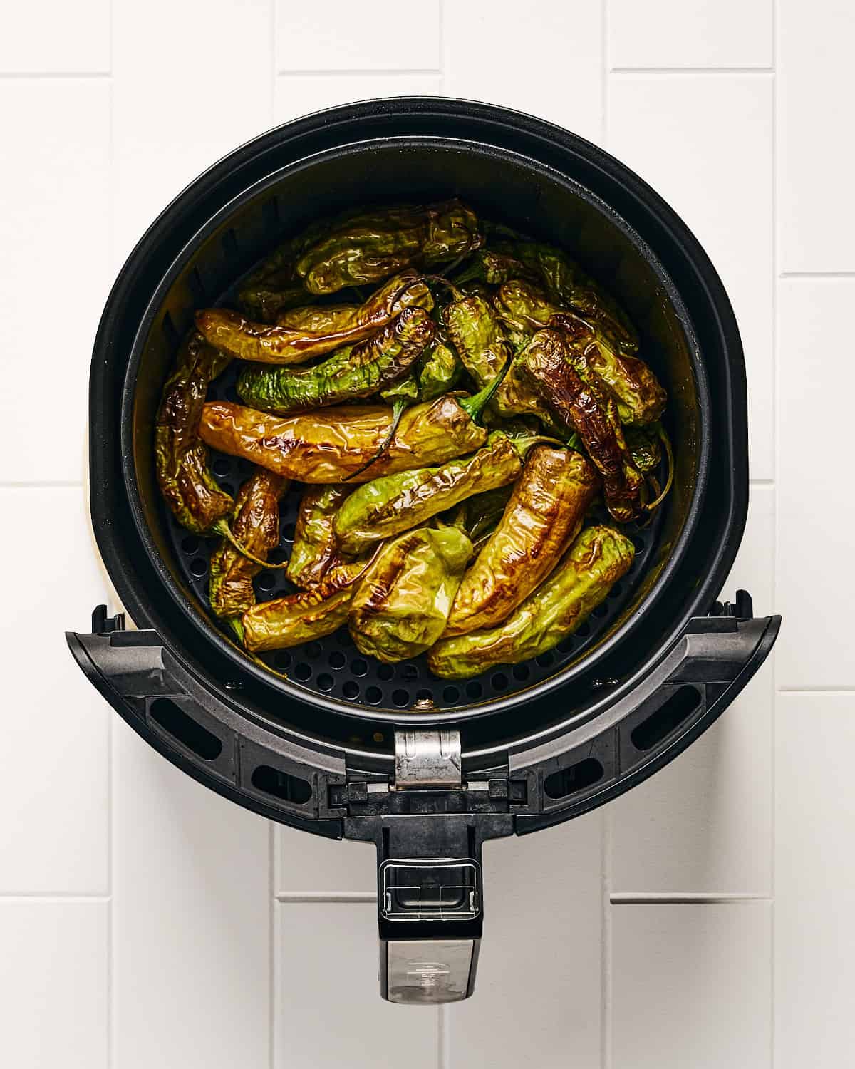 Cooked air fryer shishito peppers in air fryer basket.