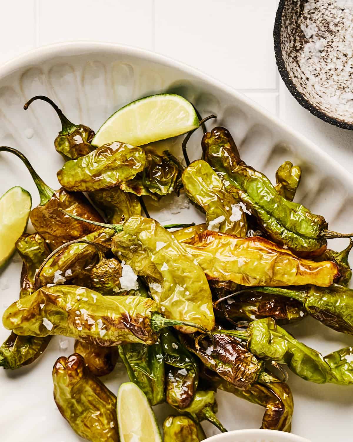 Air Fryer Shishito Peppers on a platter with wedges of lime and coarse salt.