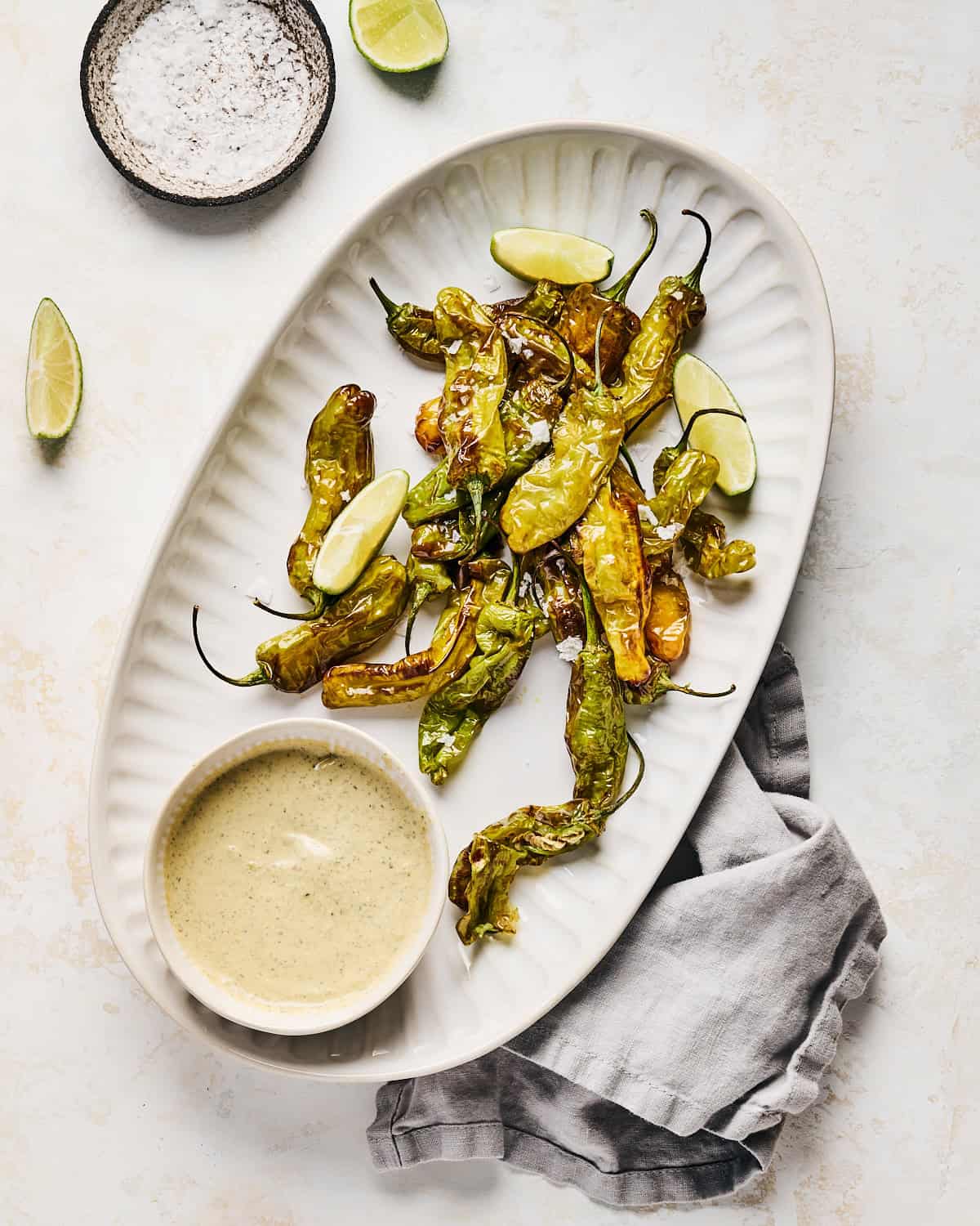 Air Fryer Shishito Peppers with lime wedges and coarse salt on a platter with dipping sauce.