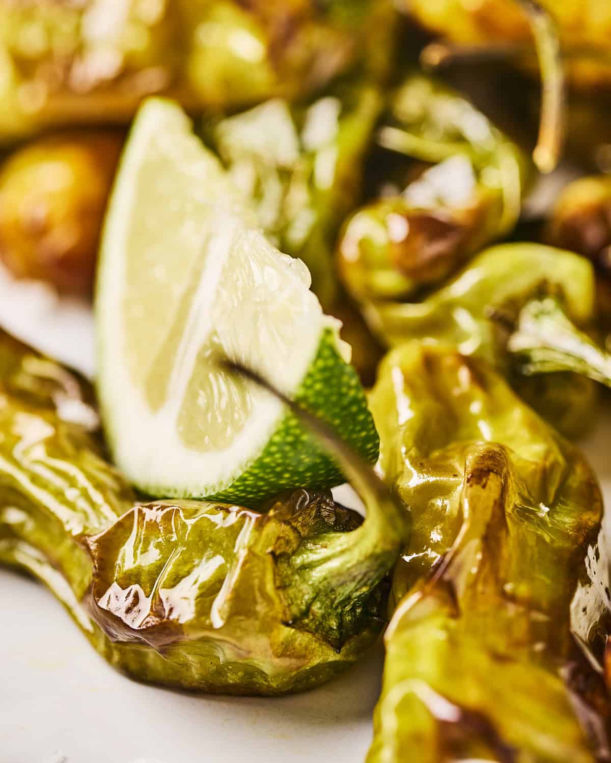 Close up of air fryer shishito peppers with lime wedge resting on top.
