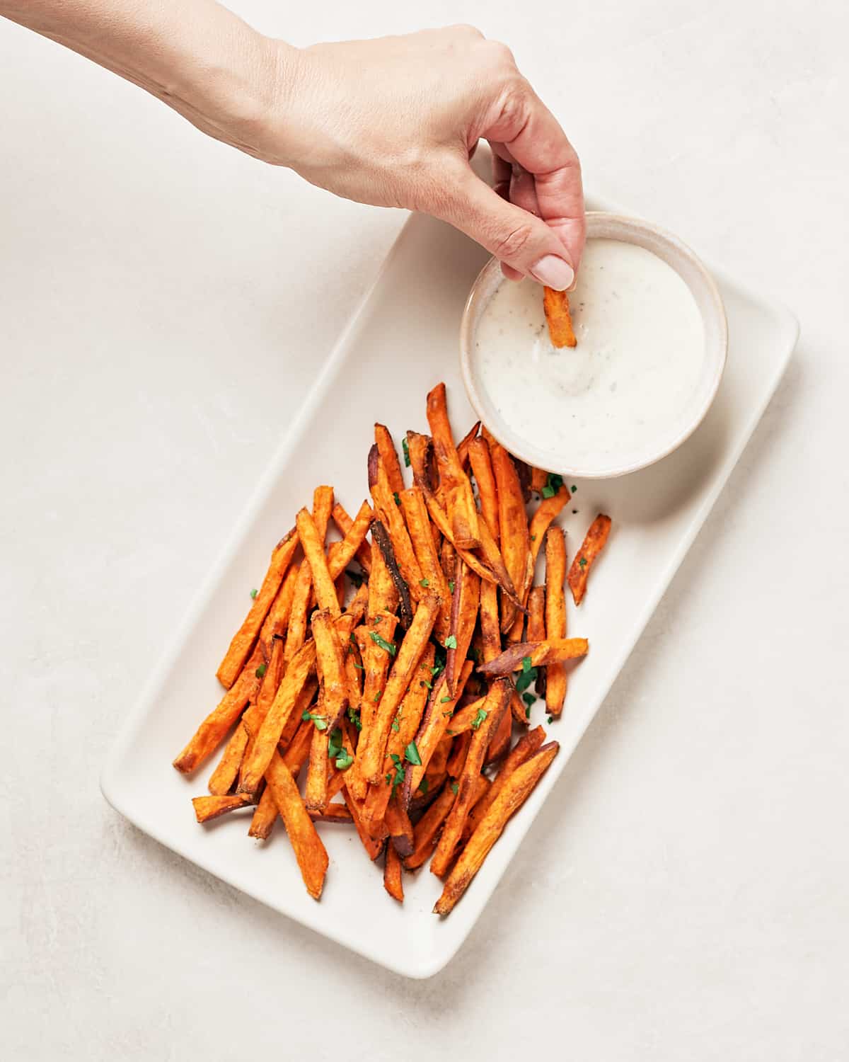 Female hand dipping a crispy baked sweet potato fries into vegan horseradish aioli.