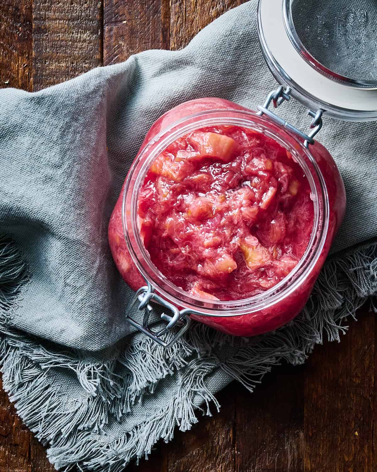 Cooked rhubarb compote in a glass jar on linen napkin.
